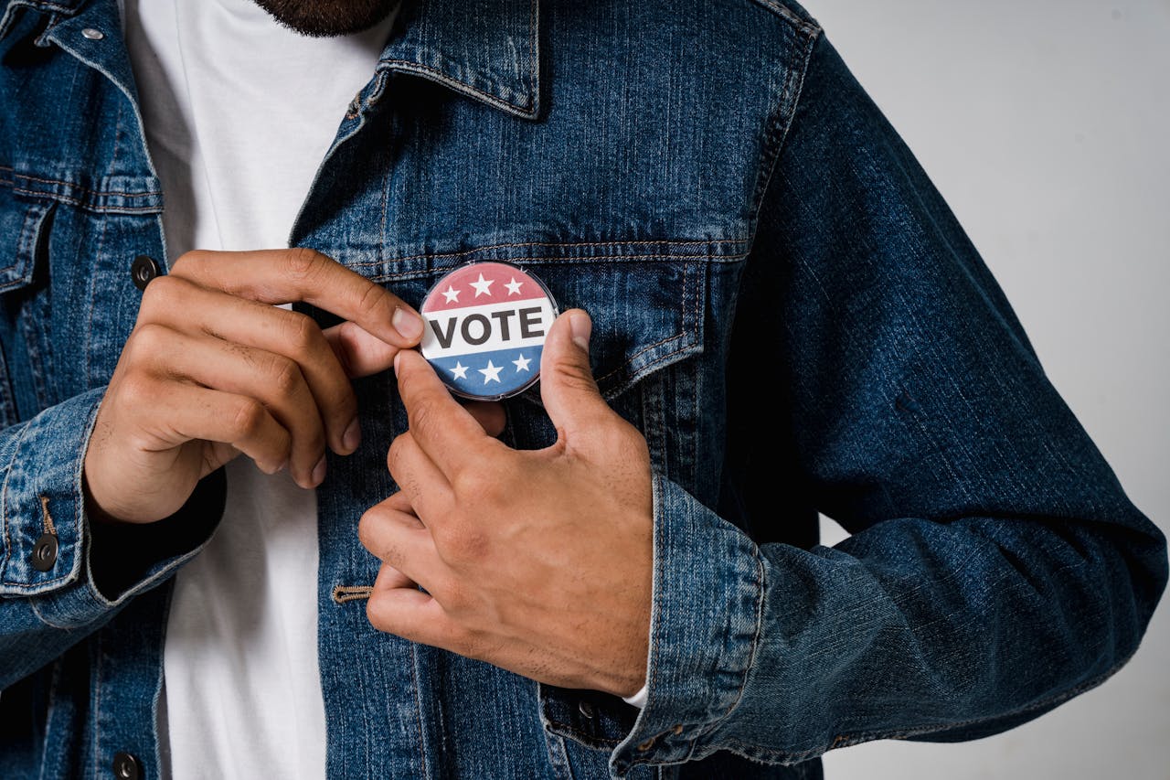 A person pinning a VOTE button on a denim jacket symbolizing civic engagement.