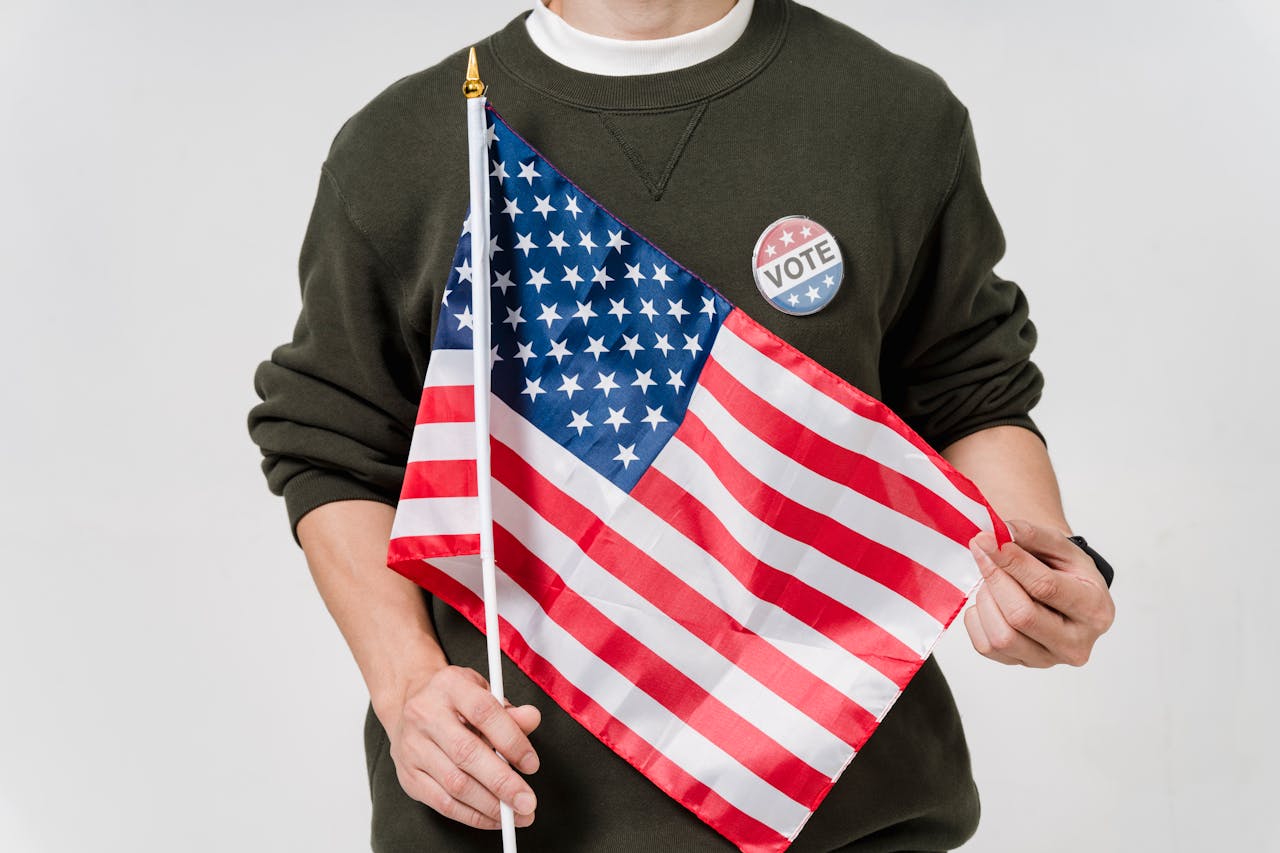 A man holding a USA flag and wearing a vote badge, symbolizing patriotism and democratic participation.